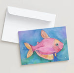 Card with a pink fish illustration on a watercolor background, accompanied by a white envelope.