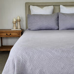 Bed with gray patterned bedding and white pillows, next to a wooden nightstand with candles.