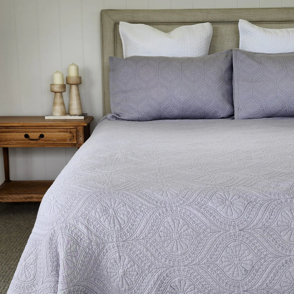 Bed with gray patterned bedding and white pillows, next to a wooden nightstand with candles.