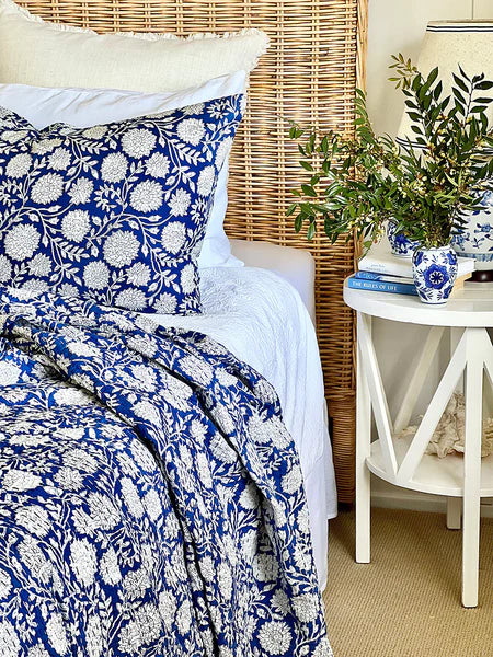 Bed with blue and white floral bedding, wicker headboard, and white nightstand with decorative items.