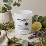 A frosted glass candle jar labeled 'Clare Makes Constance' styled on a neutral surface with eucalyptus, lavender, rosemary, a lime half, and a green lime, against a soft beige background.