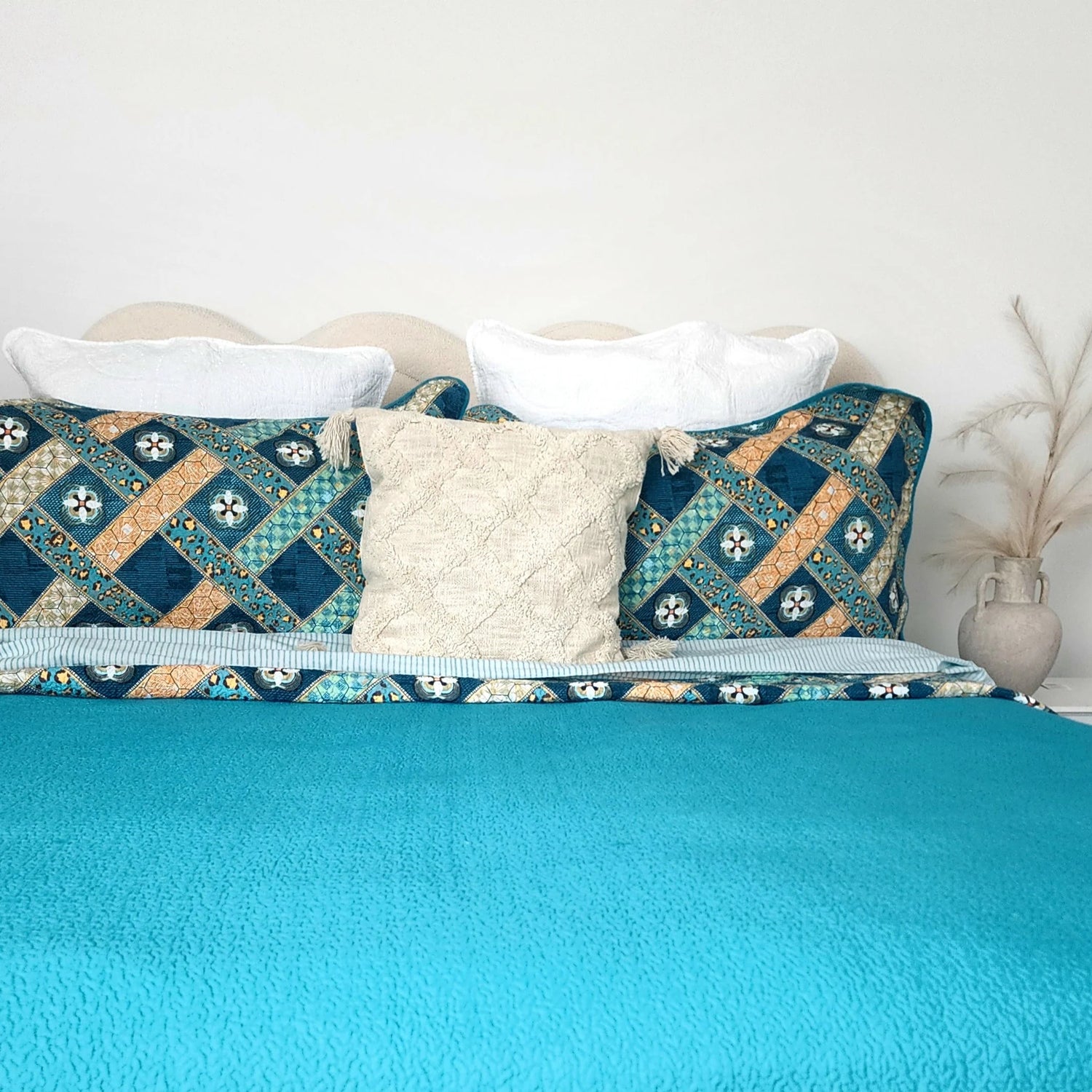 Bed with teal comforter, patterned pillows, and a white pillow.