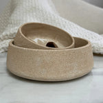 A three-tier ceramic planter in a speckled beige stoneware finish, arranged nested on a light marble surface with a textured cream knit blanket in the background.
