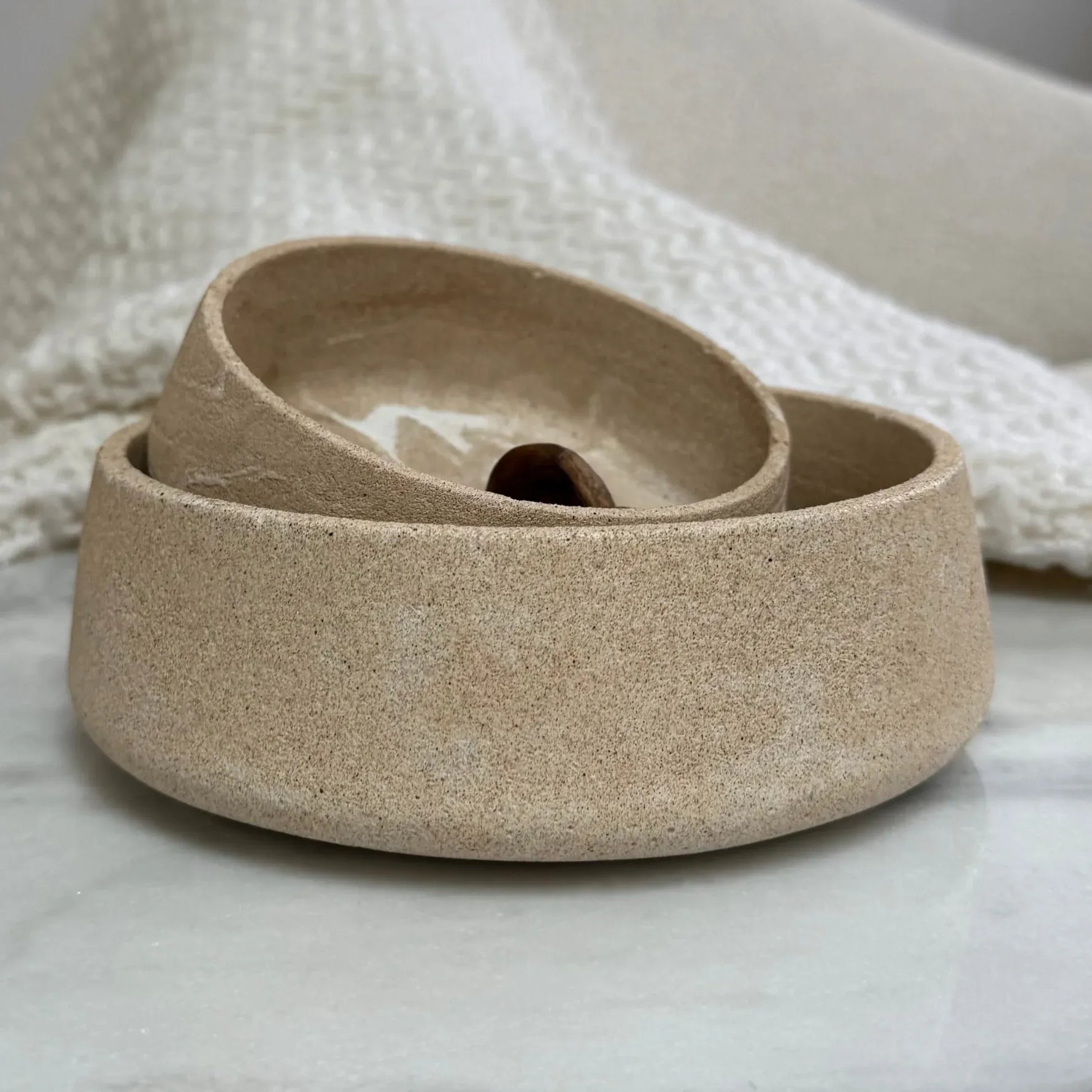 A three-tier ceramic planter in a speckled beige stoneware finish, arranged nested on a light marble surface with a textured cream knit blanket in the background.