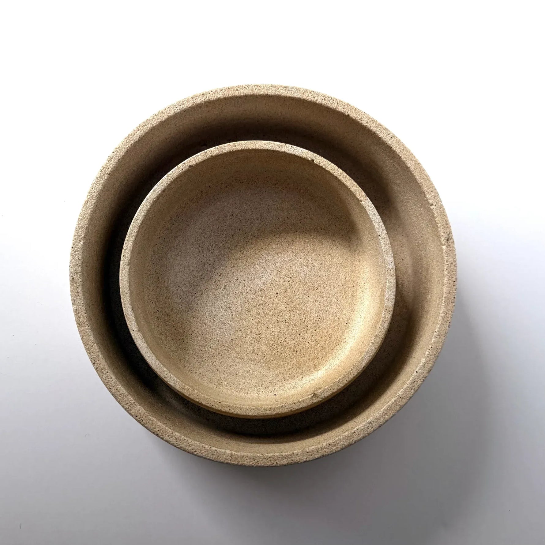 Three nested ceramic bowls in a light beige stoneware finish, photographed from directly above on a white background.