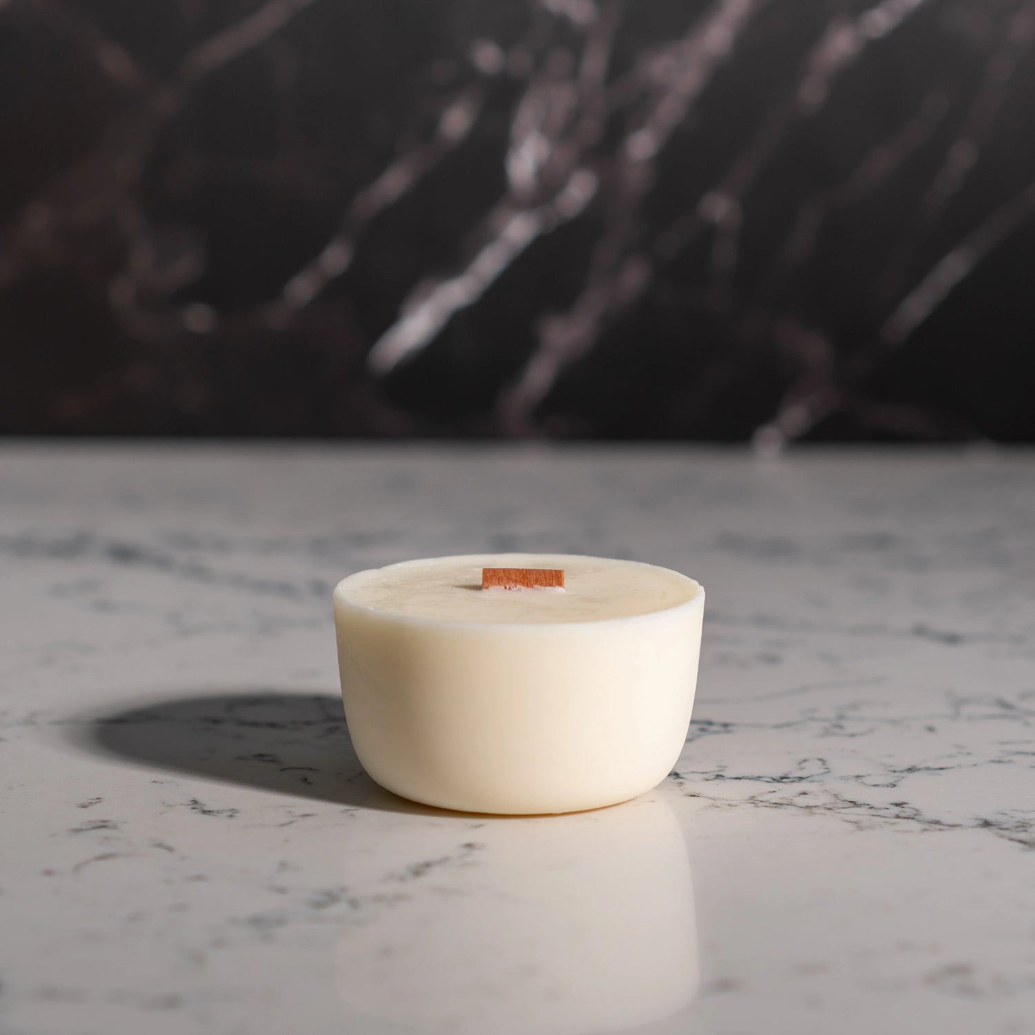 White candle in a ceramic holder on a marble surface with a dark background