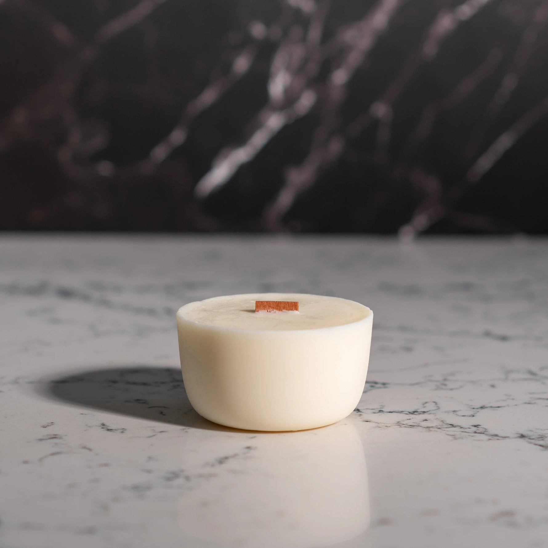 White candle in a ceramic holder on a marble surface with a dark background