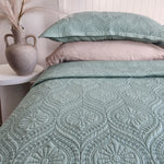Teal patterned bedding set on a bed with a side table and vase in the background.