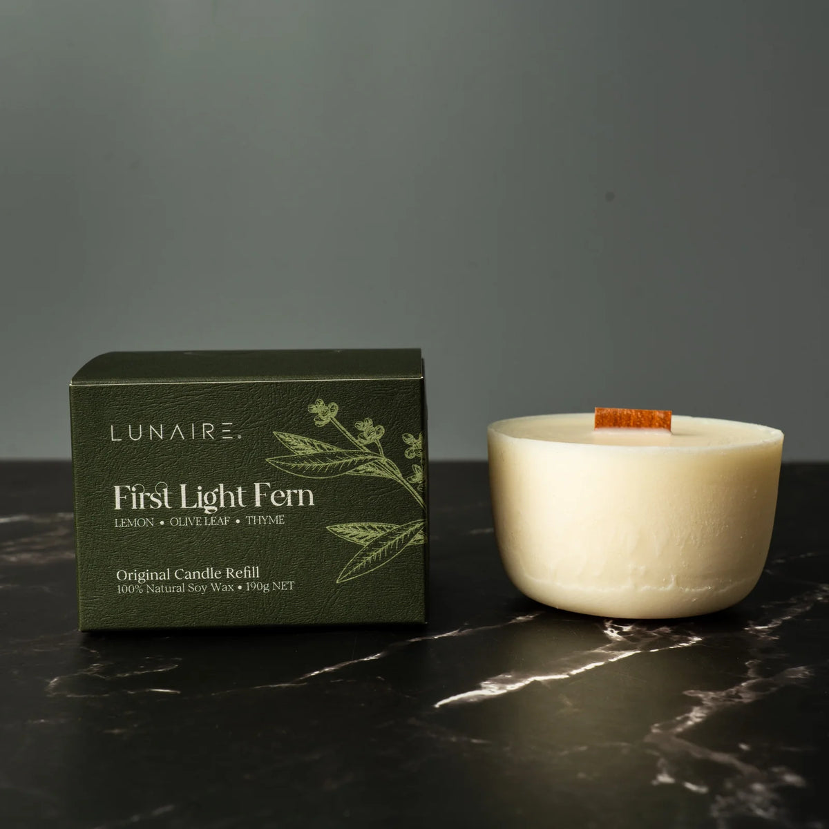 Lunaire candle and packaging on a dark surface with a gray background