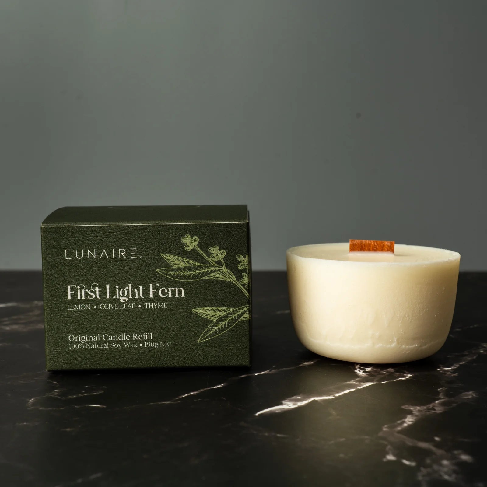 Lunaire candle and packaging on a dark surface with a gray background
