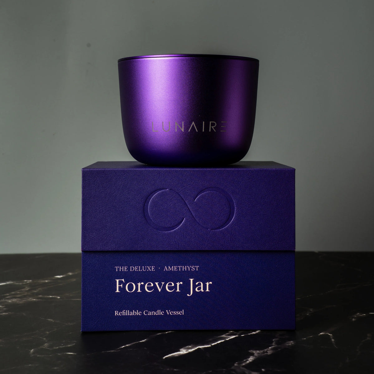 Purple candle jar with 'LUNAIRE' branding on a matching box against a dark background