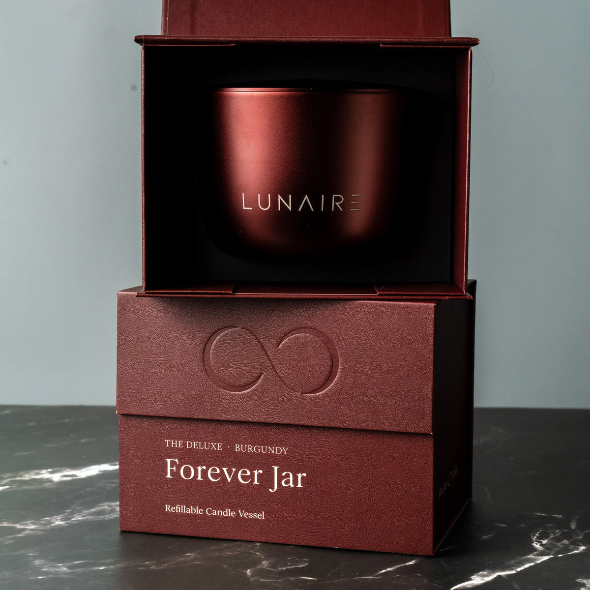 Burgundy candle vessel in a box with 'LUNAIRE' branding on a gray background