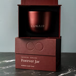 Burgundy candle vessel in a box with 'LUNAIRE' branding on a gray background