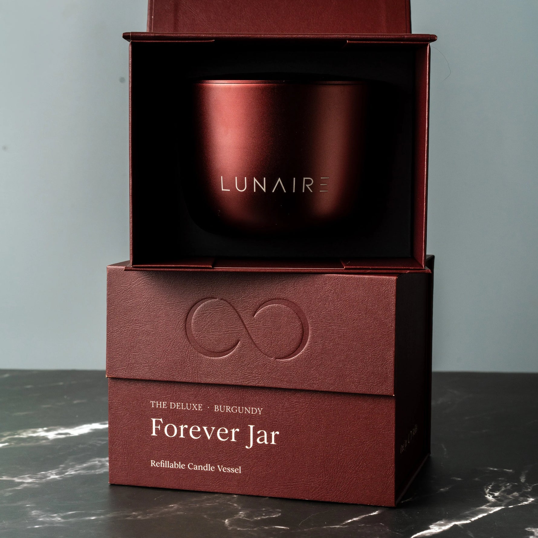 Burgundy candle vessel in a box with 'LUNAIRE' branding on a gray background