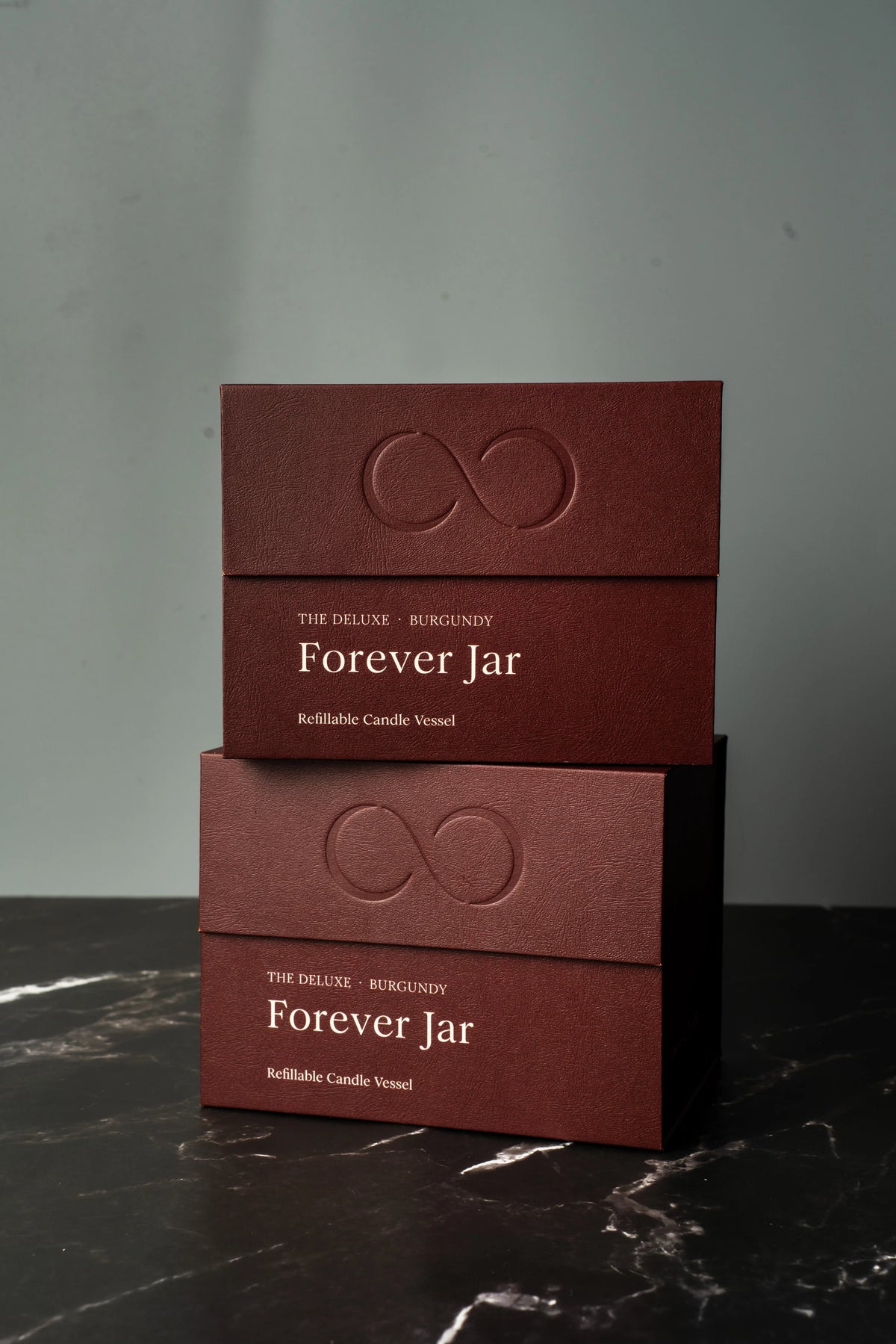 Two burgundy boxes labeled 'Forever Jar' on a dark marble surface with a gray background.