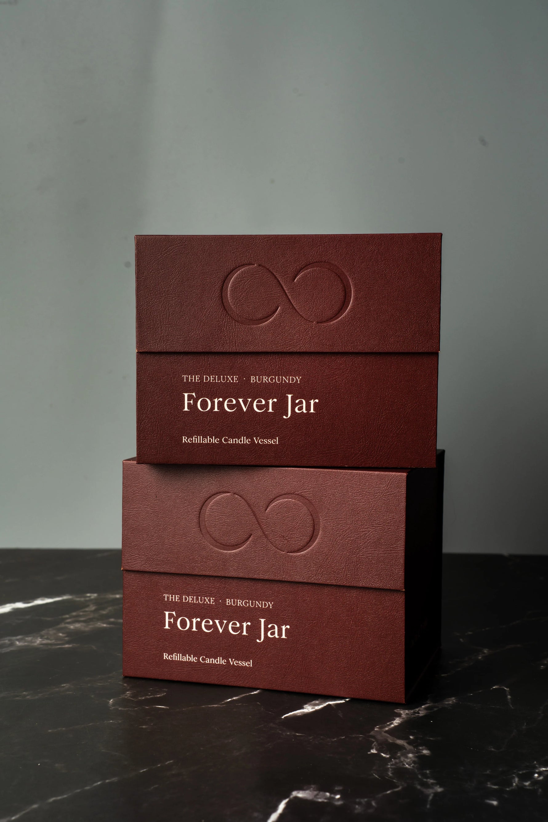 Two burgundy boxes labeled 'Forever Jar' on a dark marble surface with a gray background.