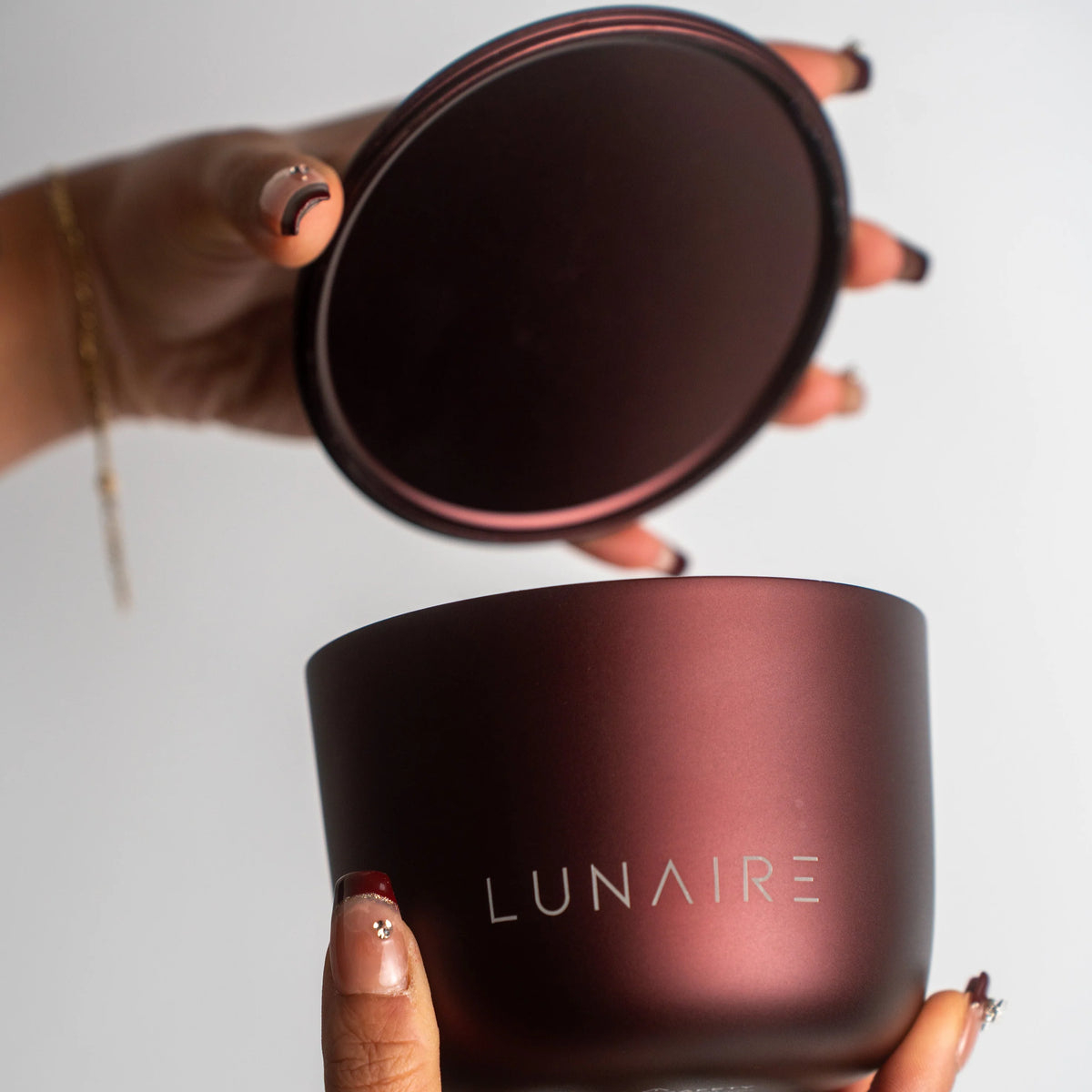 Person holding a dark purple container with 'LUNAIRE' branding against a light background
