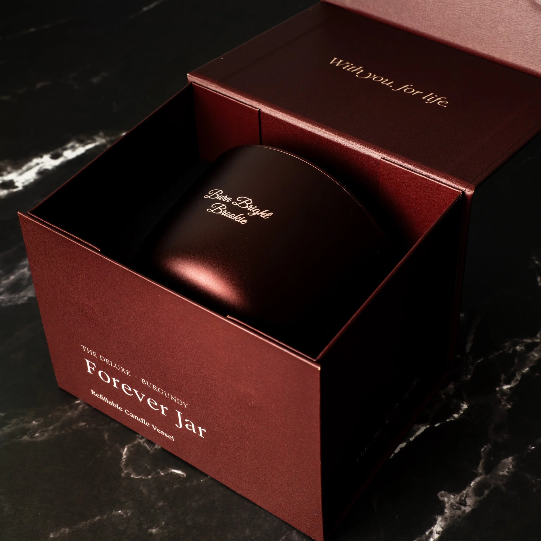 Brown candle in a matching box with 'Forever Jar' branding on a dark marble surface.
