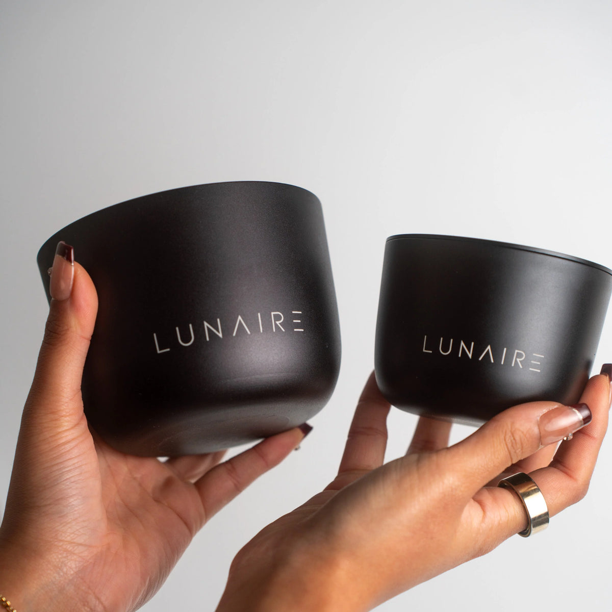 Two black containers with 'LUNAIRE' branding held by hands against a light gray background