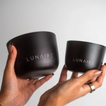 Two black containers with 'LUNAIRE' branding held by hands against a light gray background
