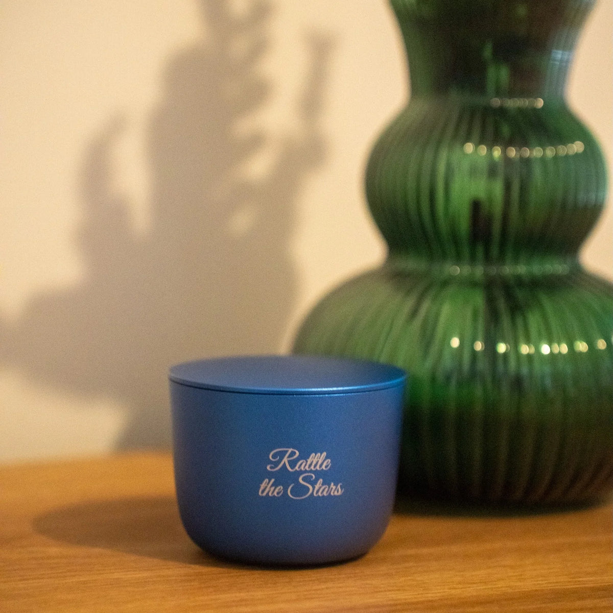 Blue container with 'Rattle the Stars' text next to a green vase on a wooden surface.
