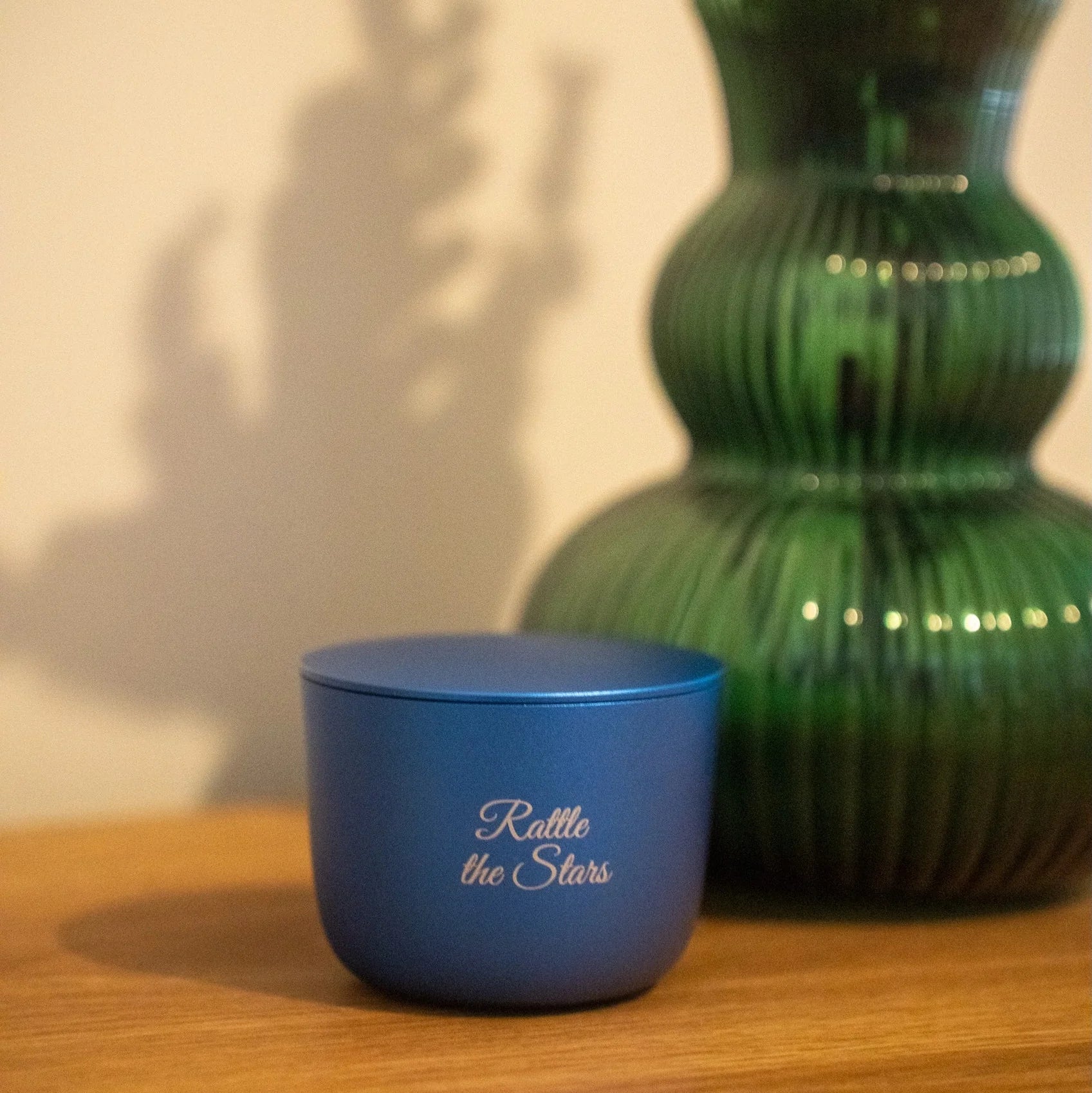 Blue container with 'Rattle the Stars' text next to a green vase on a wooden surface.