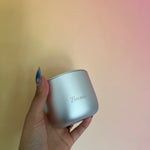 Hand holding a silver container with 'Brenda' engraved on it against a blurred background