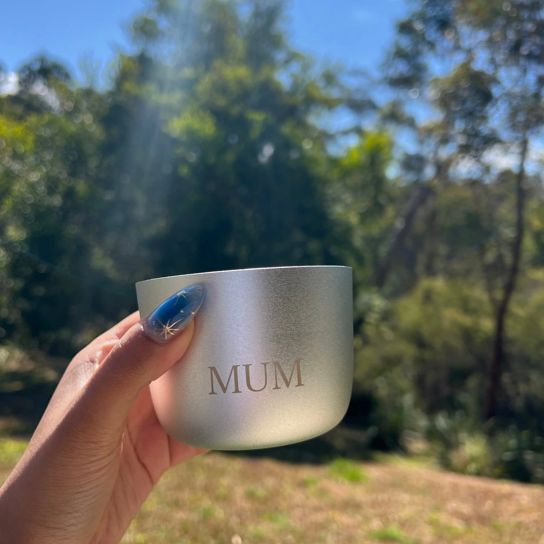 Hand holding a silver cup with 'MUM' engraved outdoors