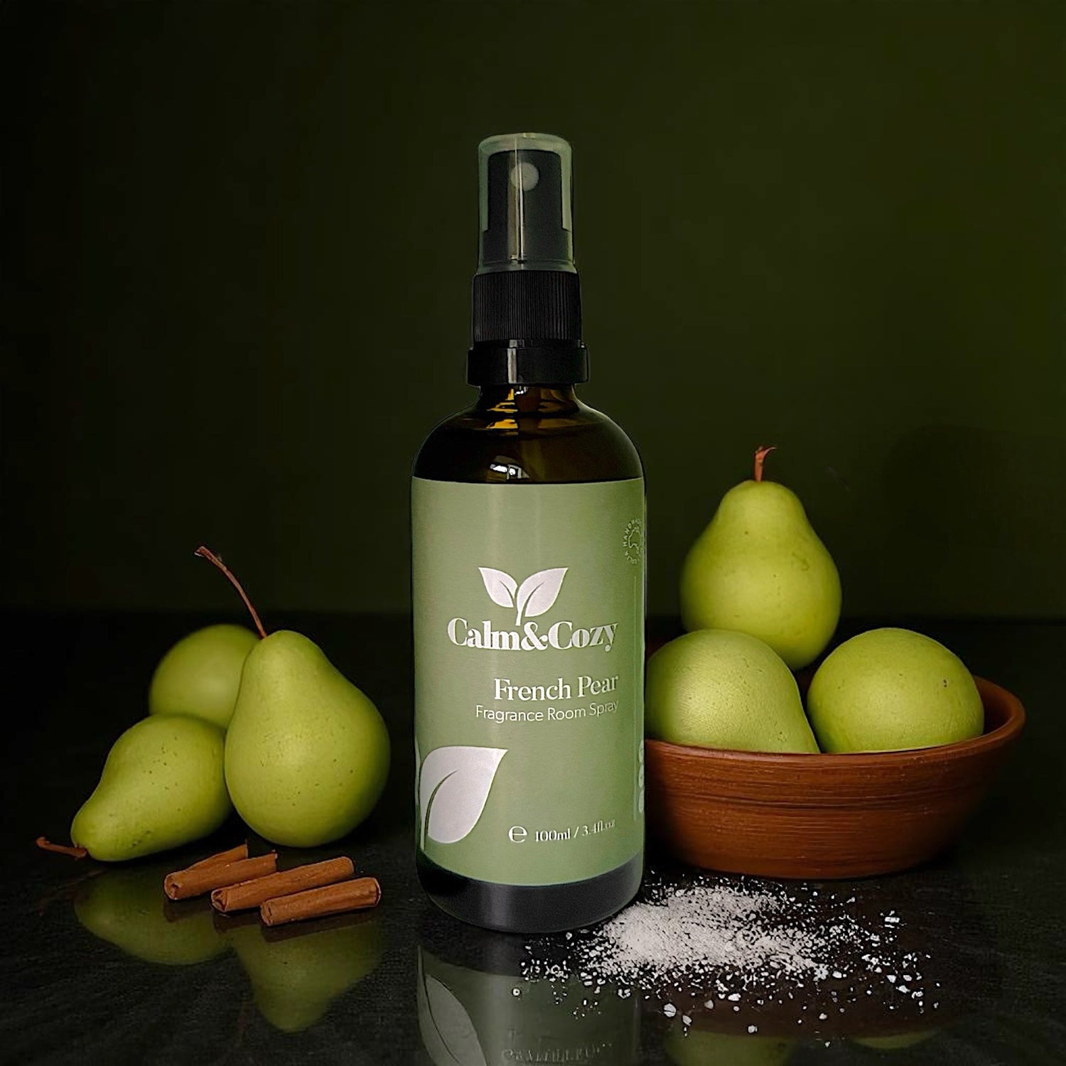 Bottle of Calm & Cozy French Pear fragrance roll-on with pears and cinnamon sticks on a dark surface