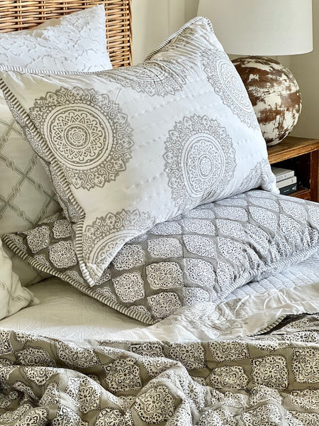 Patterned pillows and blanket on a bed with a wooden headboard.