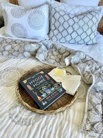 Book titled 'My Hygge Home' on a woven tray with candles and blankets on a bed.