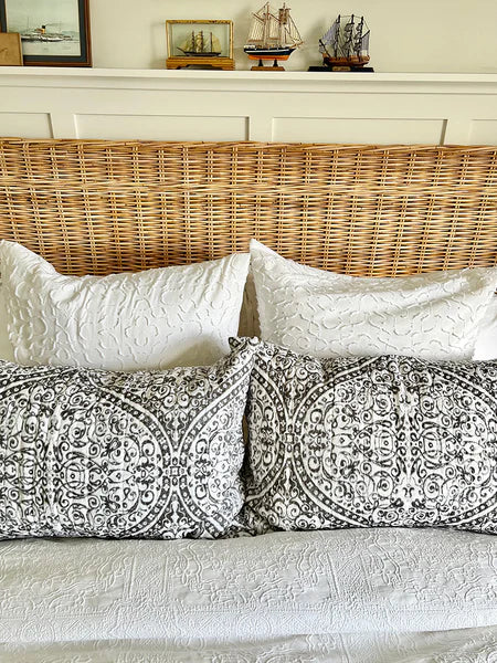 Decorative pillows on a sofa with a wicker headboard and framed pictures in the background.