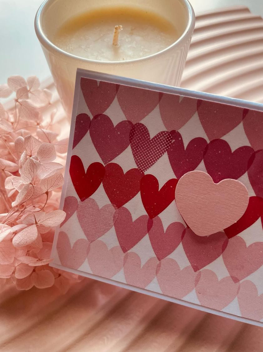 Card with heart pattern next to a candle on pink fabric