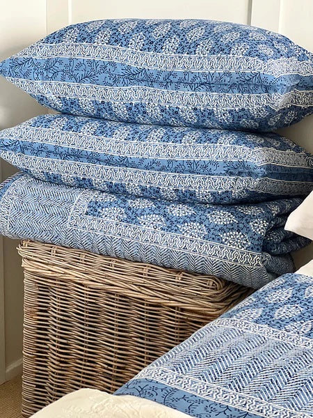 Stack of blue patterned pillows on a wicker basket against a white wall.