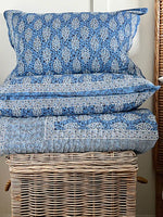 Stack of blue and white patterned pillows on a woven basket against a neutral wall.