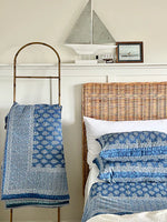 Bedroom with wicker headboard, blue patterned bedding, and decorative items on shelf.