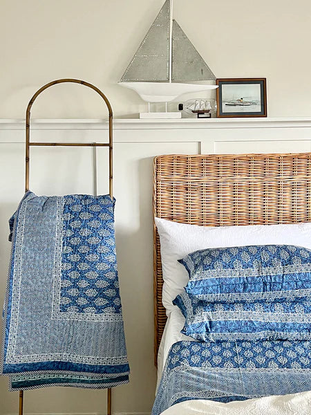 Bedroom with wicker headboard, blue patterned bedding, and decorative items on shelf.