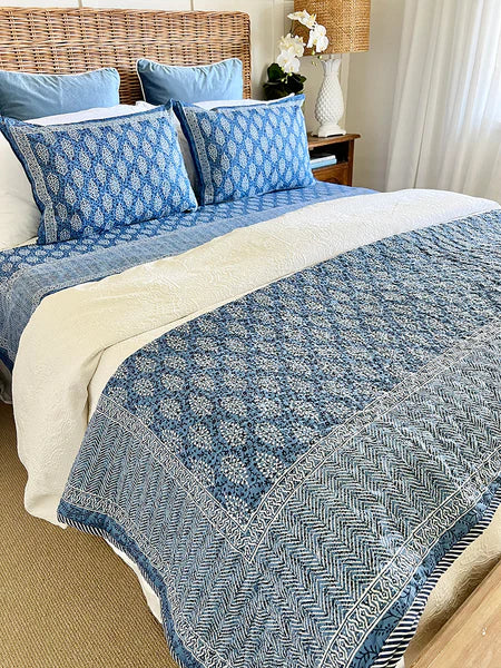Blue patterned quilt and pillows on a bed in a bedroom setting.