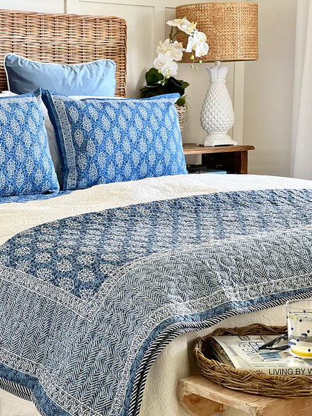 Bed with blue and white patterned bedding, pillows, and a lamp in a bedroom setting.
