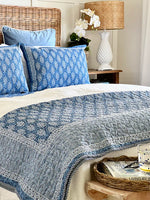 Bed with blue and white patterned bedding, pillows, and a lamp in a bedroom setting.