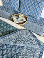 Blue patterned sofa with a woven basket and books on a wooden floor.