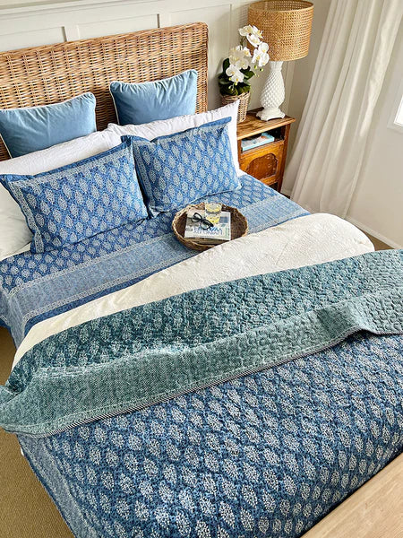 Bed with blue and white floral bedding, wicker headboard, and wooden nightstand.