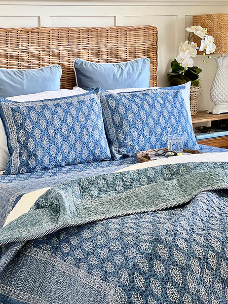 Bed with blue floral bedding and pillows in a bedroom setting.
