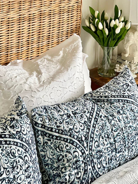 Bed with black and white patterned bedding, white pillows, and a vase of white tulips on a wooden nightstand.