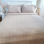 Neatly made bed with textured beige bedding and matching pillows in a bedroom setting.