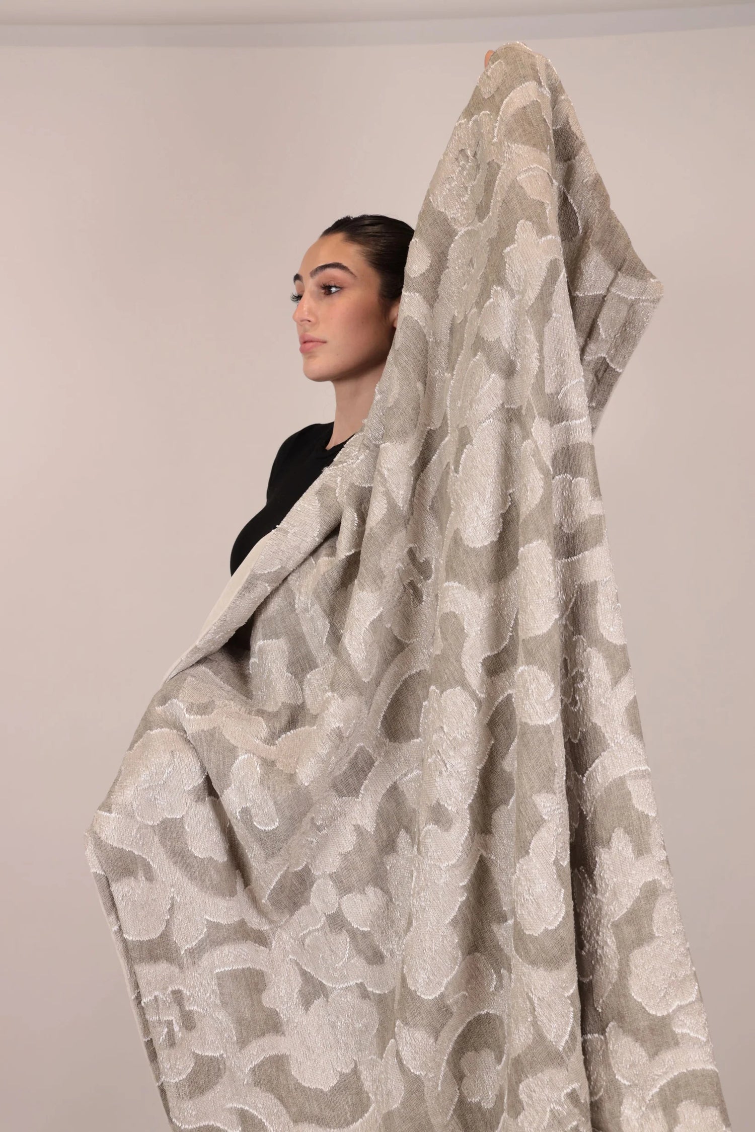Woman wearing a large beige floral-patterned blanket over her shoulders against a plain background