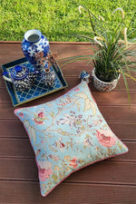 Floral pillow on a wooden surface with decorative items and plants in the background