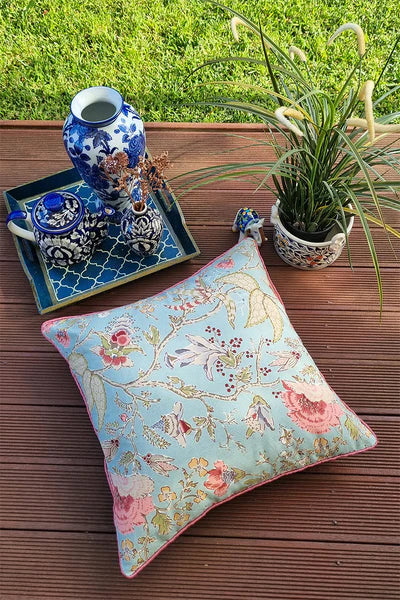 Floral pillow on a wooden surface with decorative items and plants in the background