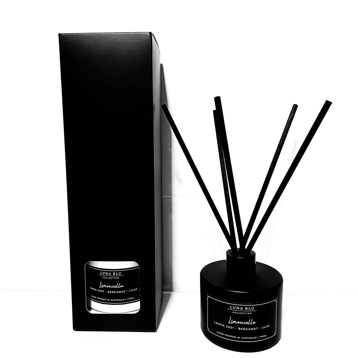 A reed diffuser set with a black cylindrical bottle, black reeds, and a tall black presentation box on a white background. The labels read 'SUKA BLUE' and 'Lemonade'.