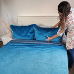 Woman arranging blue bedding on a bed in a bedroom setting